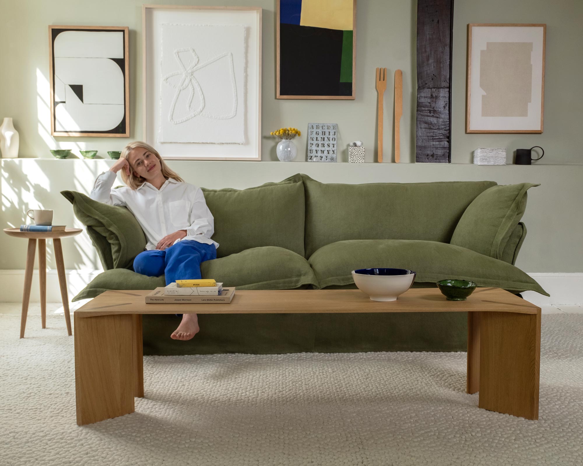 Marnie sitting on the left hand side of a malachite green sofa In front of her is a Dove coffee table styled with a large bowl and books