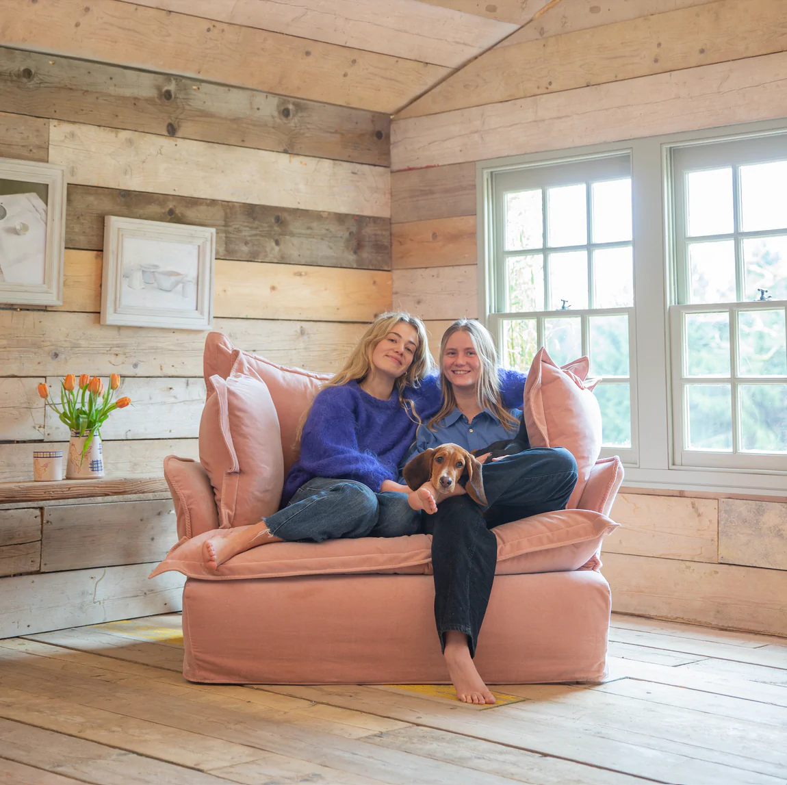 Couple sitting happily with their dog on a Maker and son plaster pink velvet loveseat in Song pillow edge.