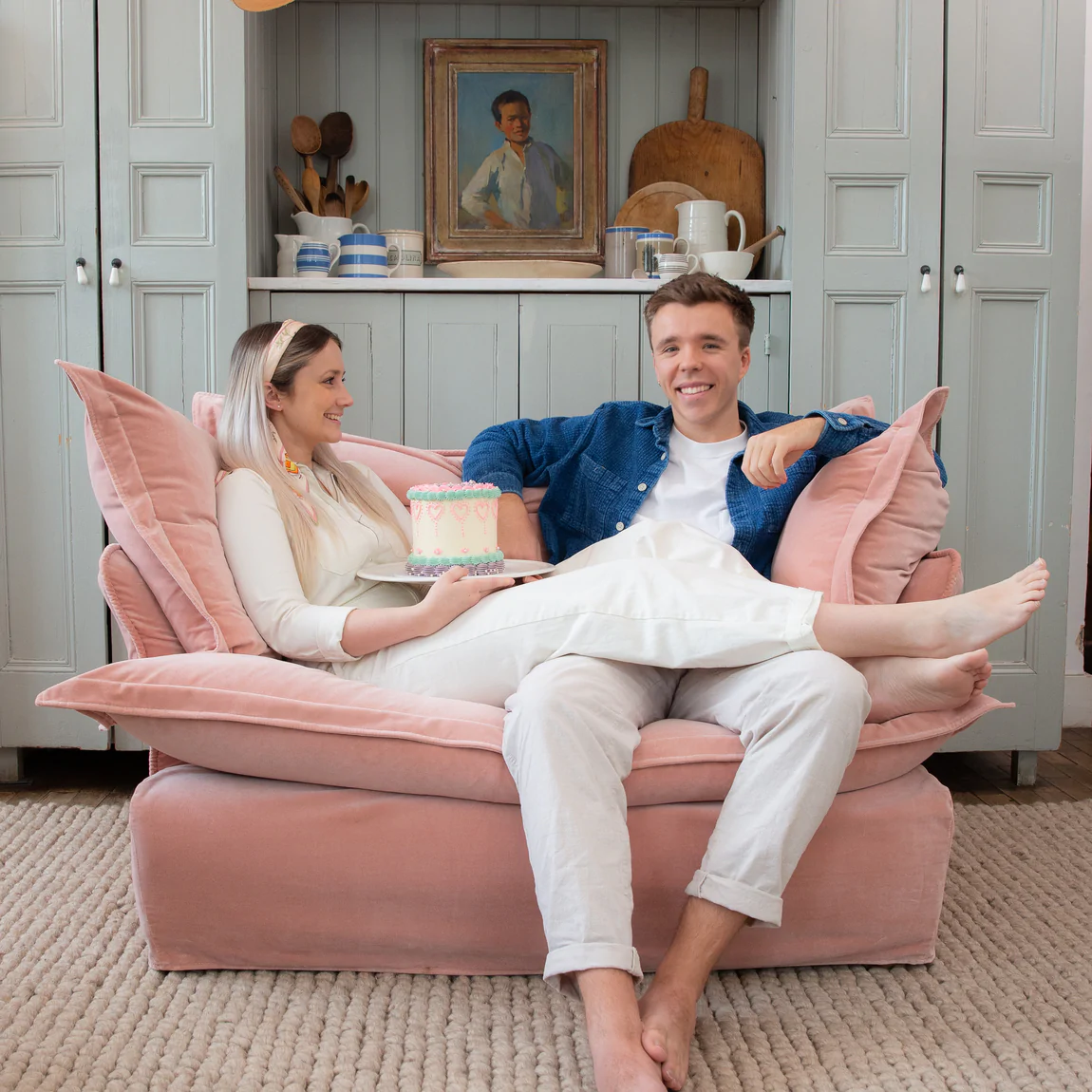 Couple sitting happily on a Maker and son plaster pink velvet loveseat in Song pillow edge